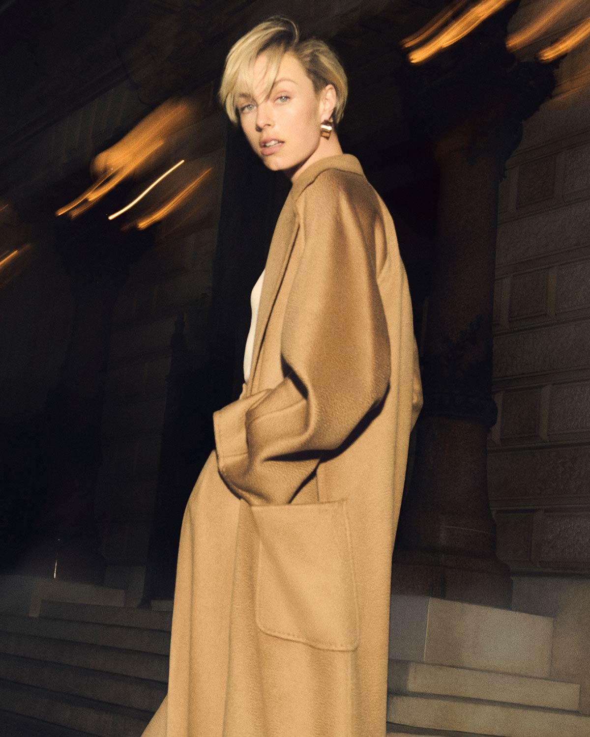 Model with Max Mara wide-fit Ludmilla icon coat in camel colour, in an evening setting.